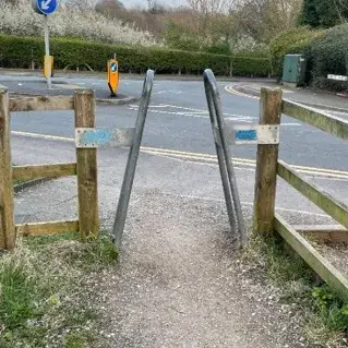 Narrow metal barrier at the end of a pedestrian path, making it difficult for wheelchairs or bikes to pass