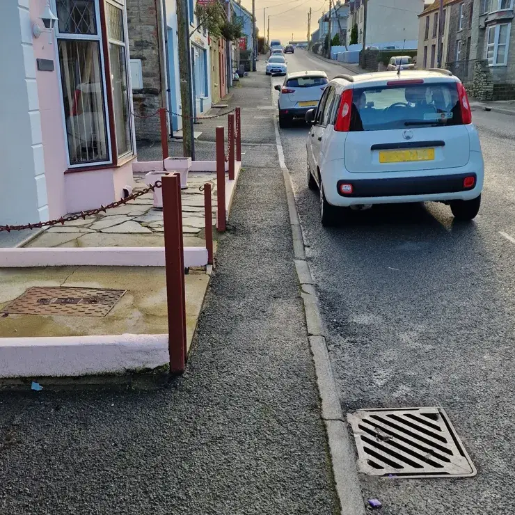 Narrow pavement partially blocked by posts and chains, limiting wheelchair access