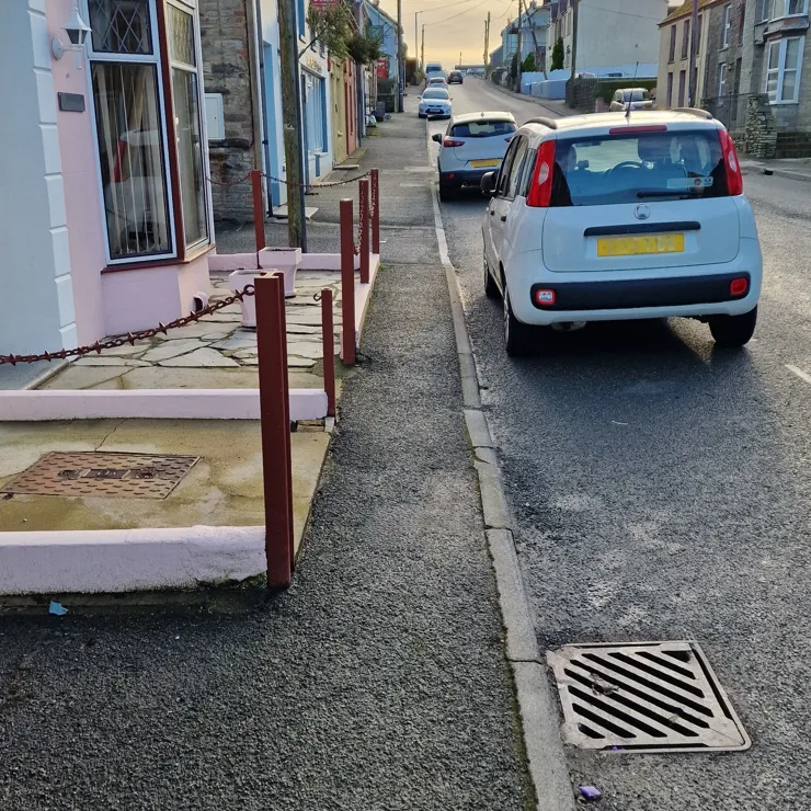 A narrow pavement runs between a row of front-garden posts and the road.
