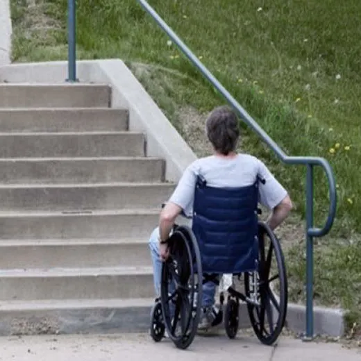 A wheelchair user faces a flight of concrete steps with handrails.